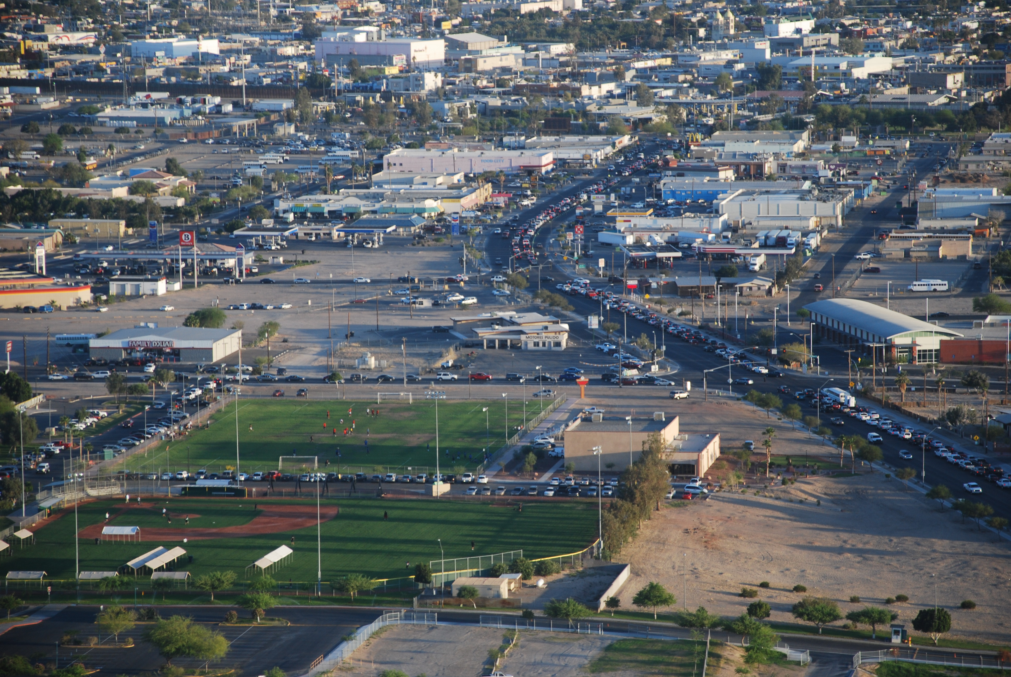 A large field featuring a baseball diamond surrounded by heavy traffic on nearby roads.