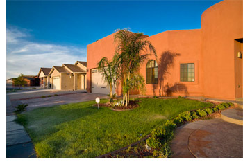 A spacious home surrounded by a large yard and several tall palm trees under a clear blue sky.